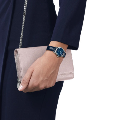 Une femme portant la montre Tissot Le Locle 29mm, cadran bleu, boîtier argent, bracelet cuir bleu.