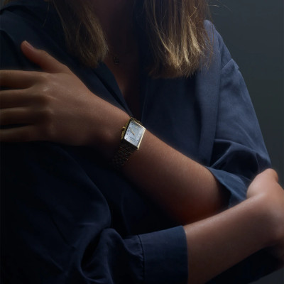 Une femme portant la montre Raymond Weil Toccata carrée, cadran nacré, bracelet en or jaune