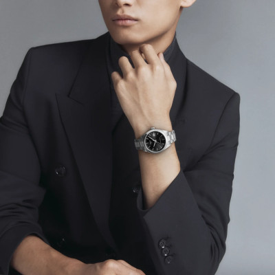 Montre Tissot Gentleman 38 mm à cadran noir et bracelet en acier argenté, portée au poignet avec une veste noire.