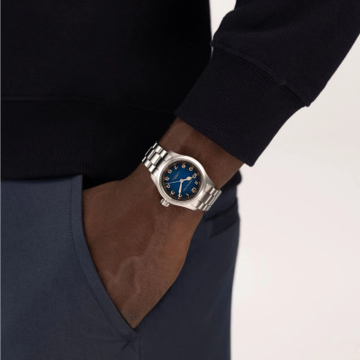 Montre Hamilton Khaki Field Murph à cadran bleu et bracelet métallique argenté, portée au poignet avec une tenue sombre.